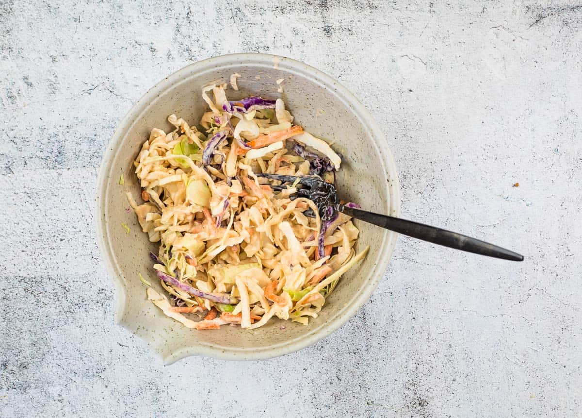 A bowl of coleslaw with vegetables and a fork.