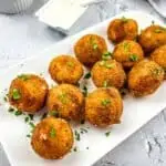 Sauerkraut balls on a plate with sauce in the background.