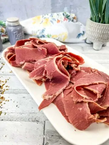 Homemade corned beef sliced thinly and on a white platter.