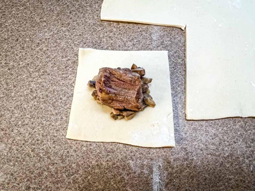 A square of puff pastry topped with the mushroom mixture and a cube of beef.
