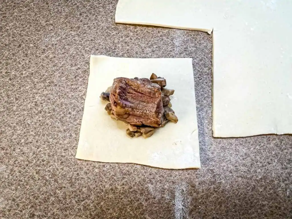 A square of puff pastry topped with the mushroom mixture and a cube of beef.