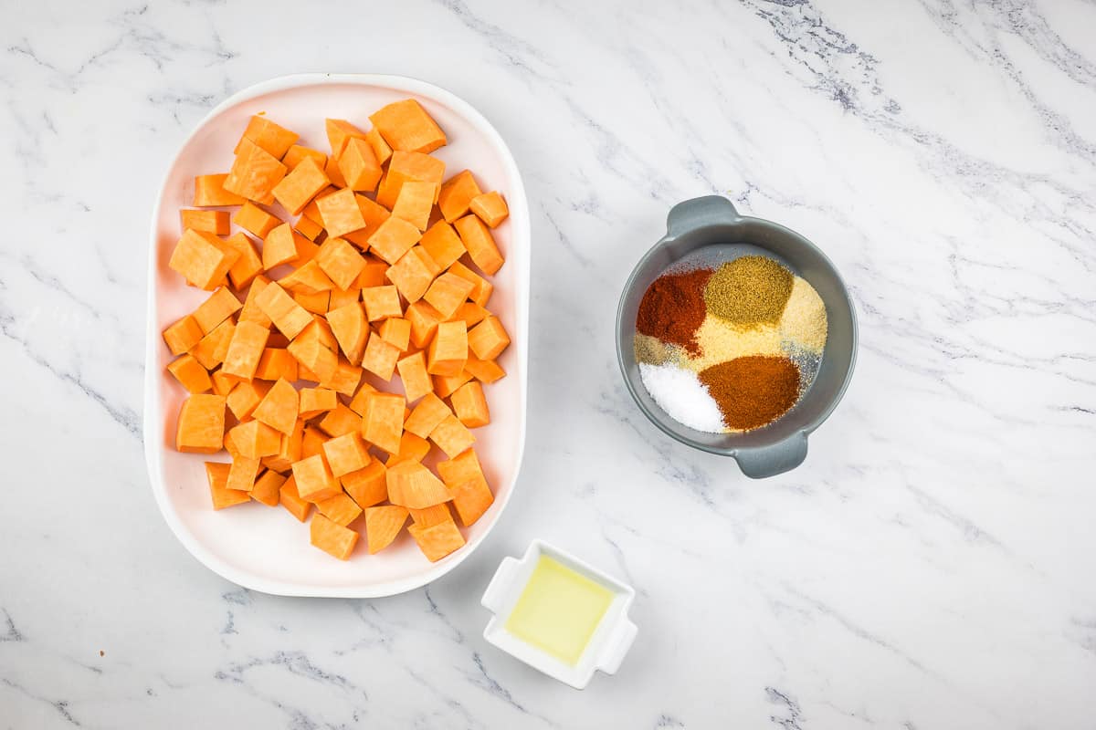 The spices to make air fryer sweet potato cubes in a bowl with the potatoes nearby.