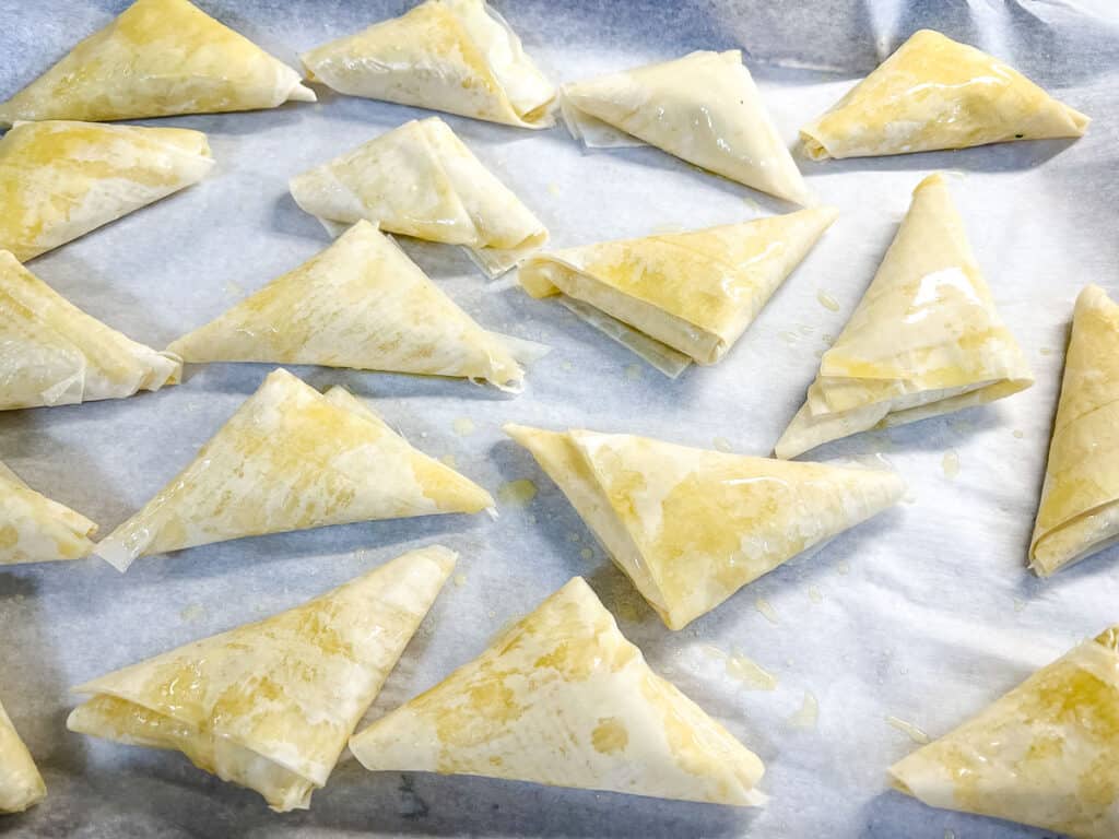 Unbaked Crab Spanakopita triangles on a baking sheet.