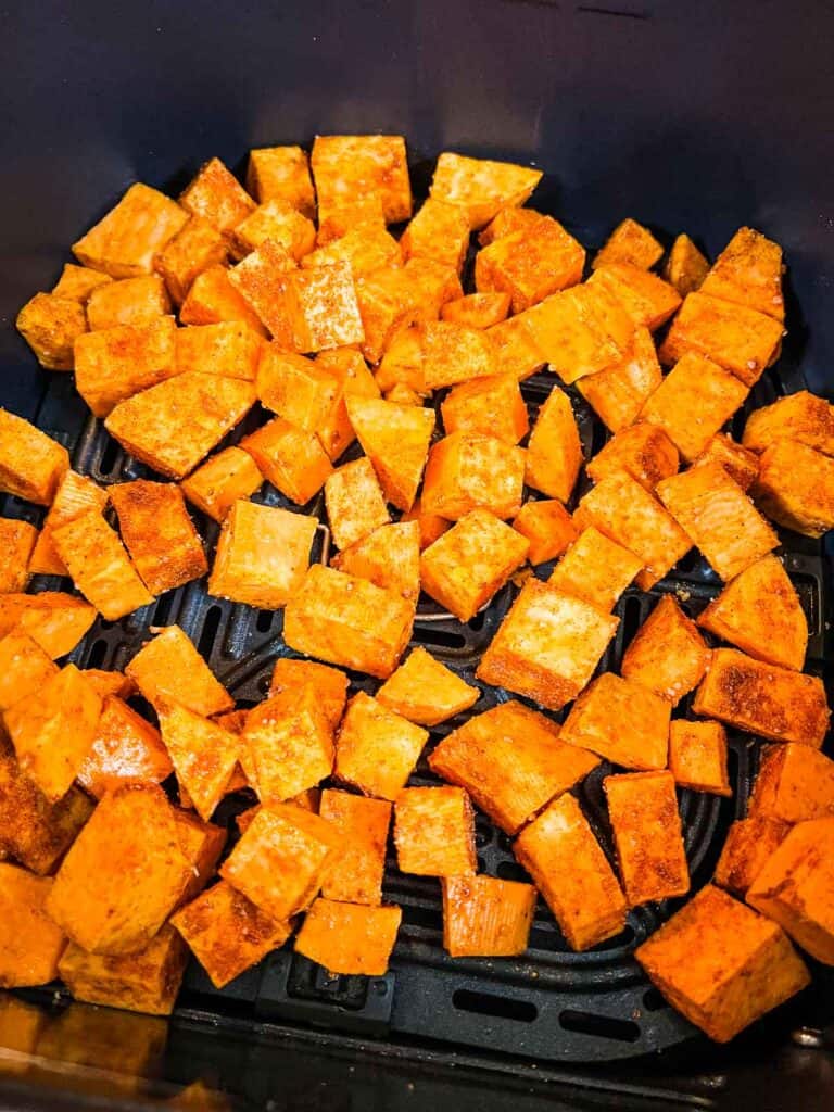 Air fryer sweet potato cubes coated with seasoning are arranged in a basket, ready for cooking.