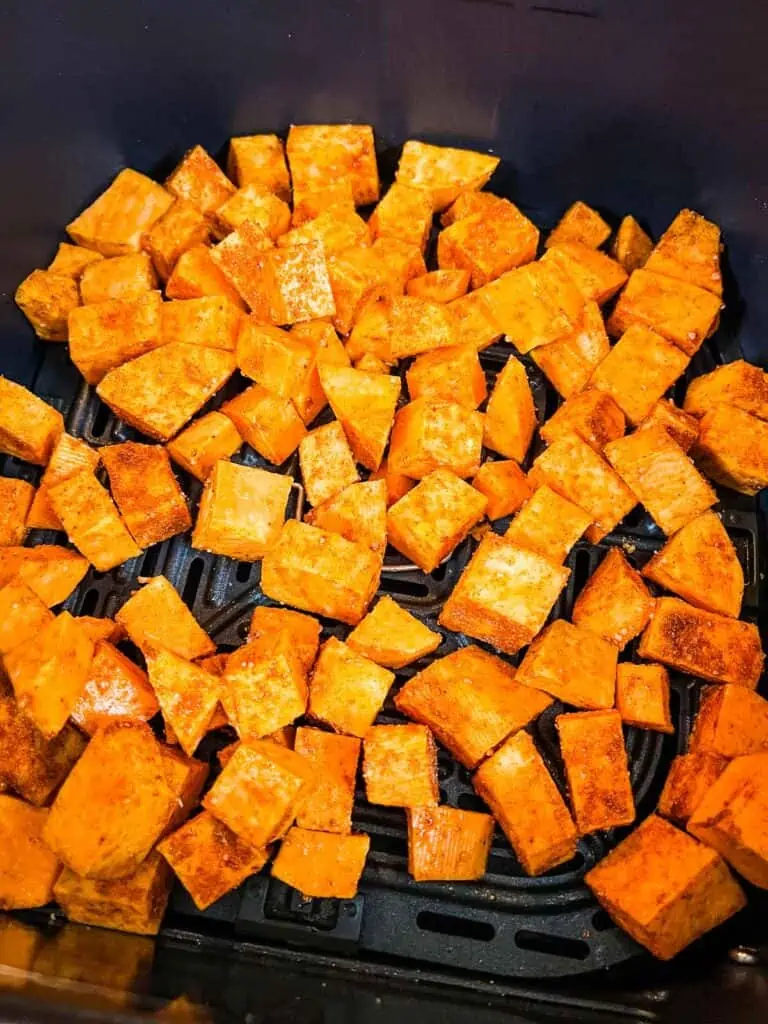 Air fryer sweet potato cubes coated with seasoning are arranged in a basket, ready for cooking.