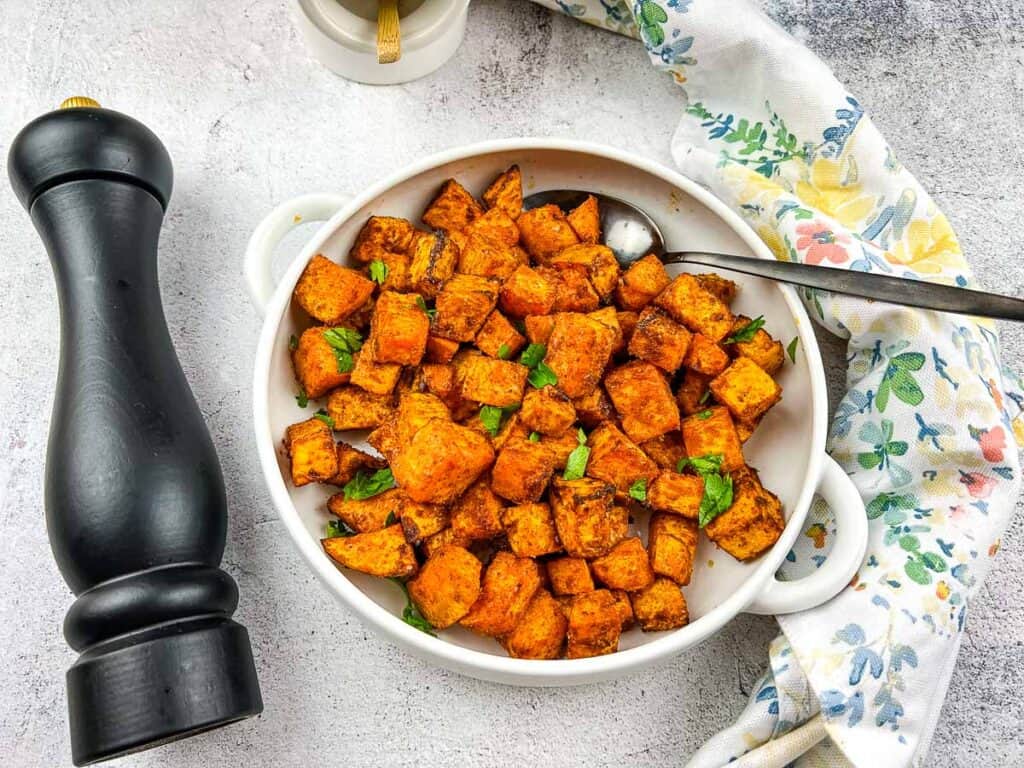 A top-down shot of air fryer sweet potato cubes in a serving bowl with a pepper grinder on the side.