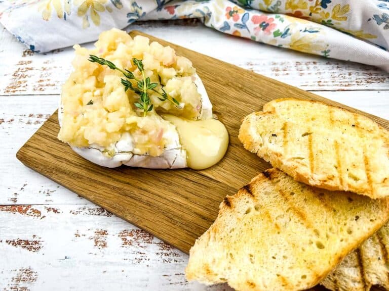 Baked brie with apple ginger chutney on a cutting board.