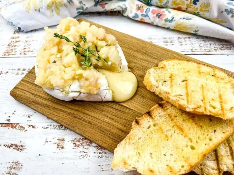 Baked brie with apple ginger chutney on a cutting board.