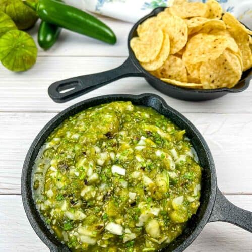 Roasted tomatillo salsa in a black cast iron dish with chips in the background.