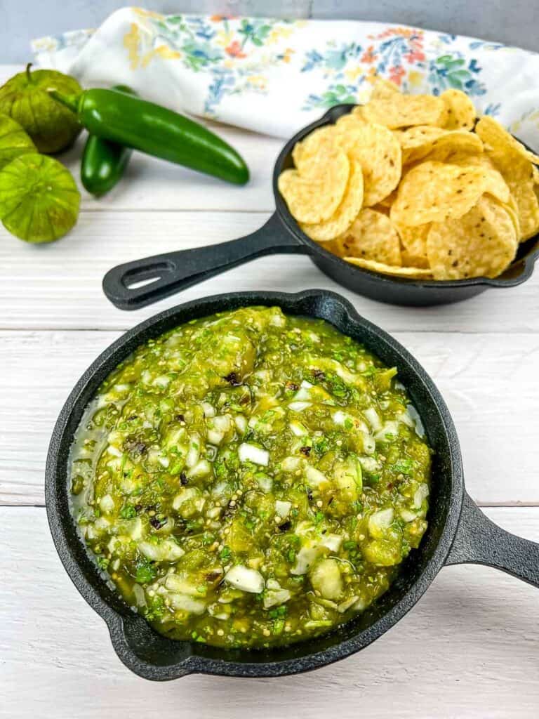Roasted tomatillo salsa in a black cast iron dish with chips in the background.