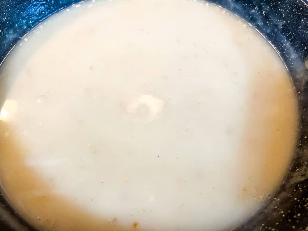 A close-up of a bowl filled with a creamy, light-colored liquid, possibly a soup, batter, or sauce&mdash;reminiscent of the rich base used in carrots au gratin.