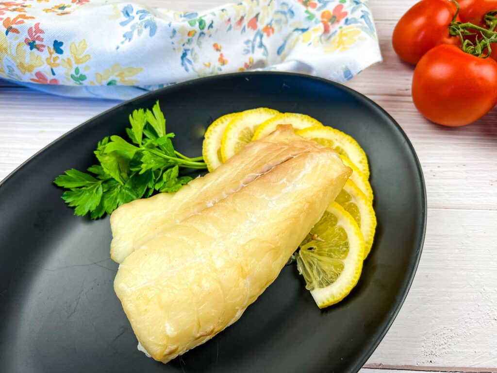 Smoked cod filet on a black plate with lemon.