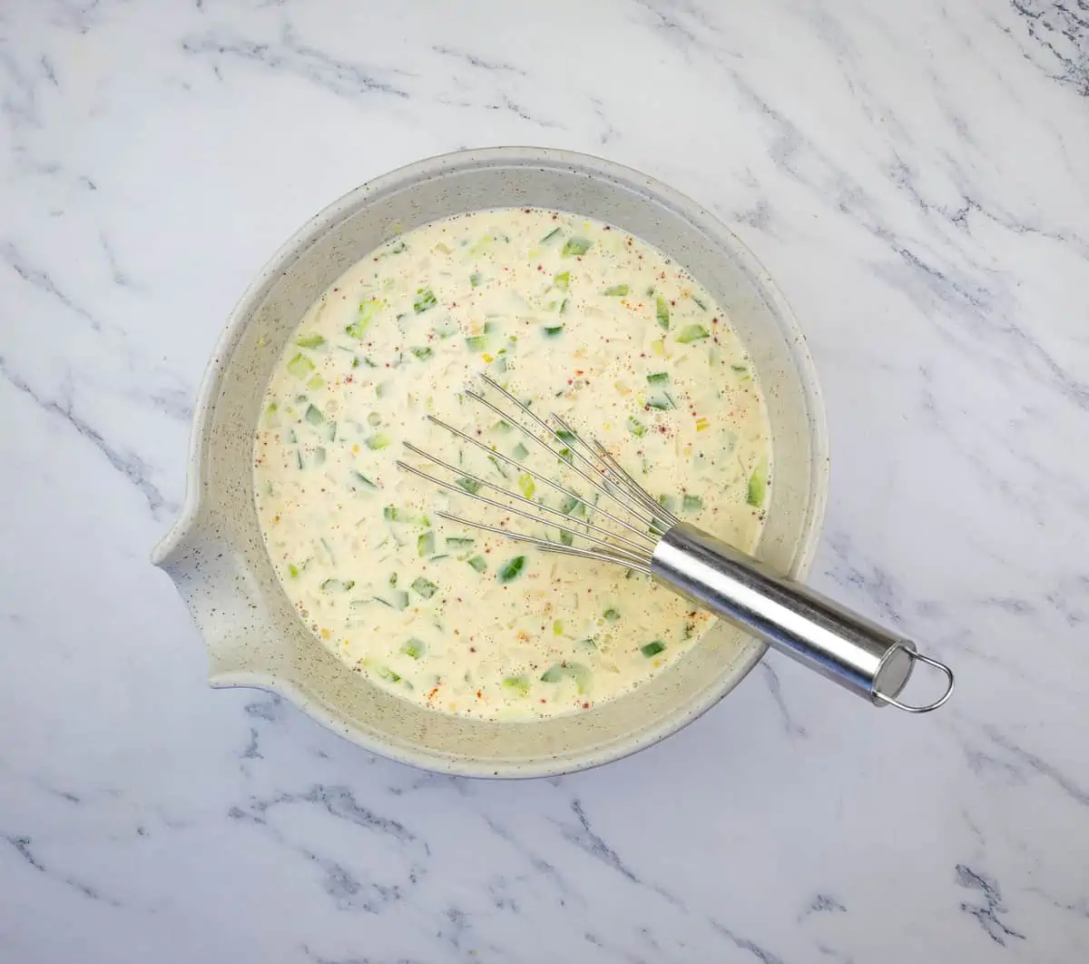 Whisking the eggs, milk, onion, peppers and seasoning in a bowl.