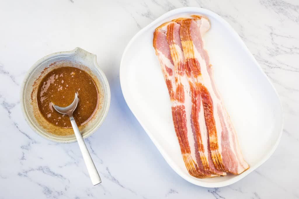 Brown sugar, syrup and spices mixed in a bowl next to the raw bacon.
