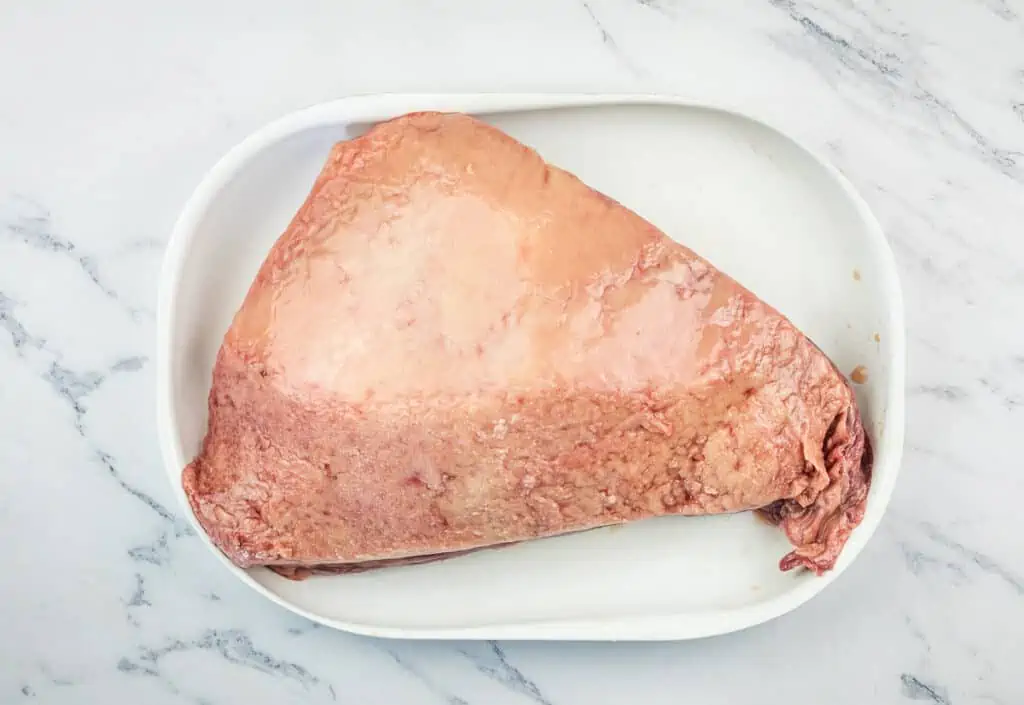 Raw picanha roast on a white plate.