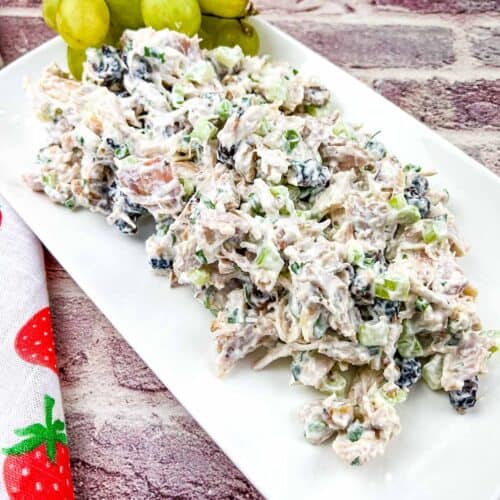 Chicken salad with cranberries and walnuts on a white platter with grapes.