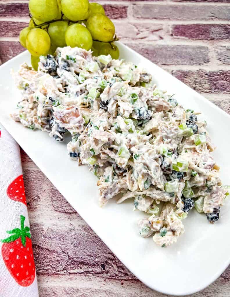 Chicken salad with cranberries and walnuts on a white platter with grapes.