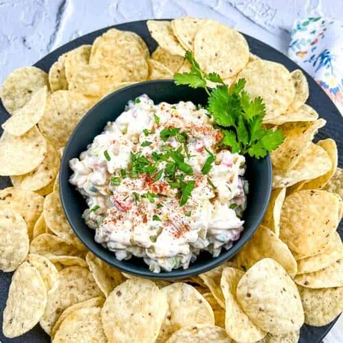 Cold corn dip in a black bowl with tortilla chips around it.