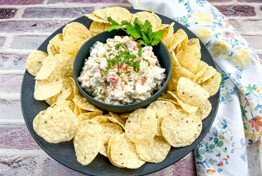 Cold corn dip in a black bowl surrounded by tortilla chips.