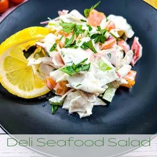Deli Seafood Salad on a black plate with a slice of lemon.