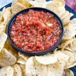 Food processor salsa in a black dish surrounded by tortilla chips.
