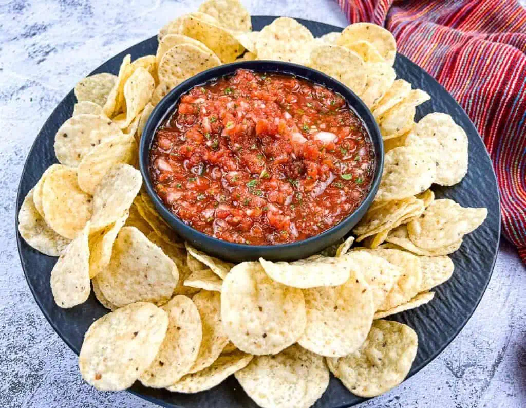 Food processor salsa in a black dish with tortilla chips around it.
