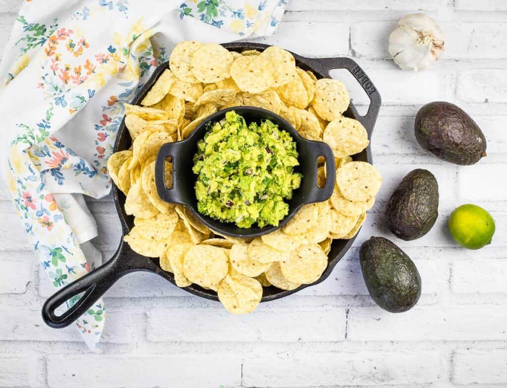 A top-down shot of guacamole in a black dish with tortilla chips.