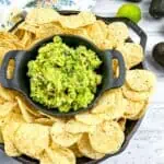 Guacamole in a black dish surrounded by tortilla chips.