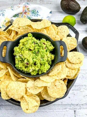 Guacamole in a black dish surrounded by tortilla chips.