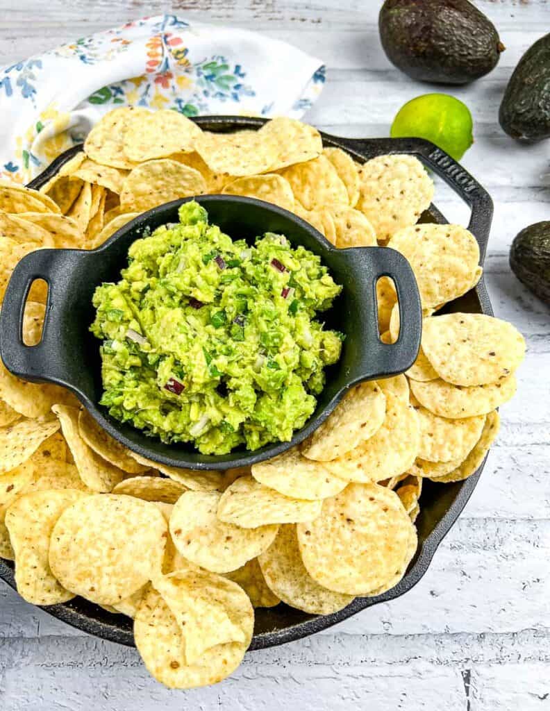 Guacamole in a black dish surrounded by tortilla cihps.