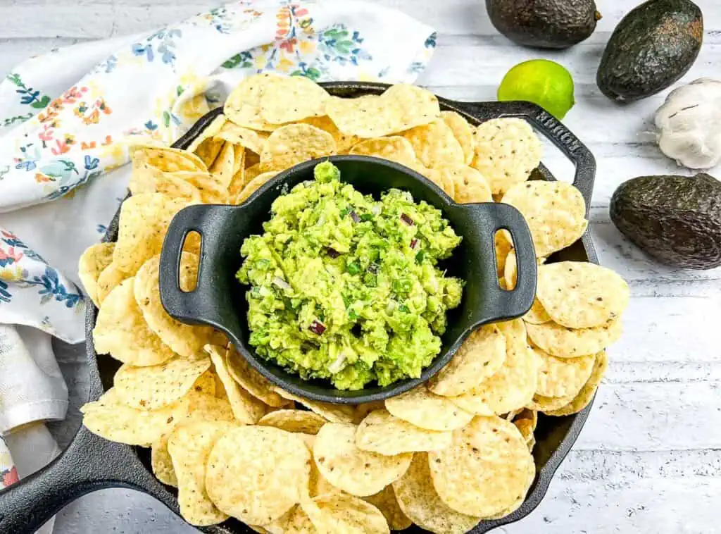 Guacamole in a black dish surrounded by tortilla chips.