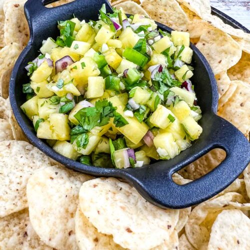 Pineapple salsa in a black serving dish surrounded by tortilla chips.