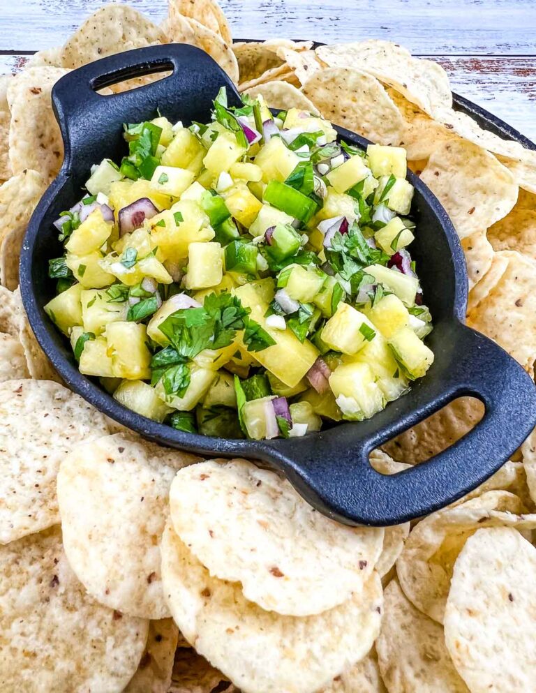 Pineapple salsa in a black serving dish surrounded by tortilla chips.