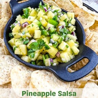 Pineapple salsa in a black dish with tortilla chips.