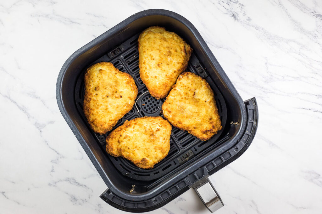 Chicken cutlets in an air fryer basket.