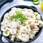 Salmon Pasta Salad in a bowl with lemon and cucumbers in the background.