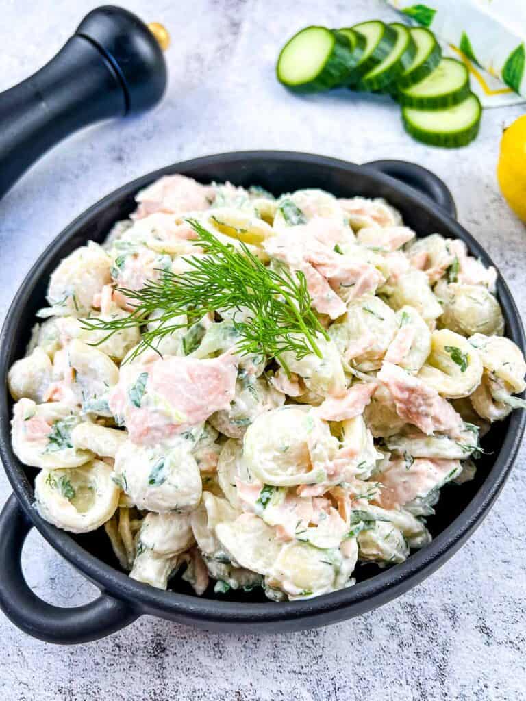 Salmon Pasta Salad in a bowl with lemon and cucumbers in the background.