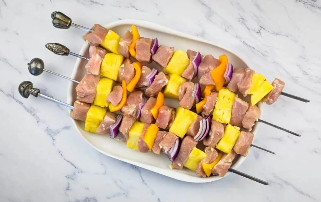 Uncooked Smoked Pork and Pineapple Kabobs on a white plate.