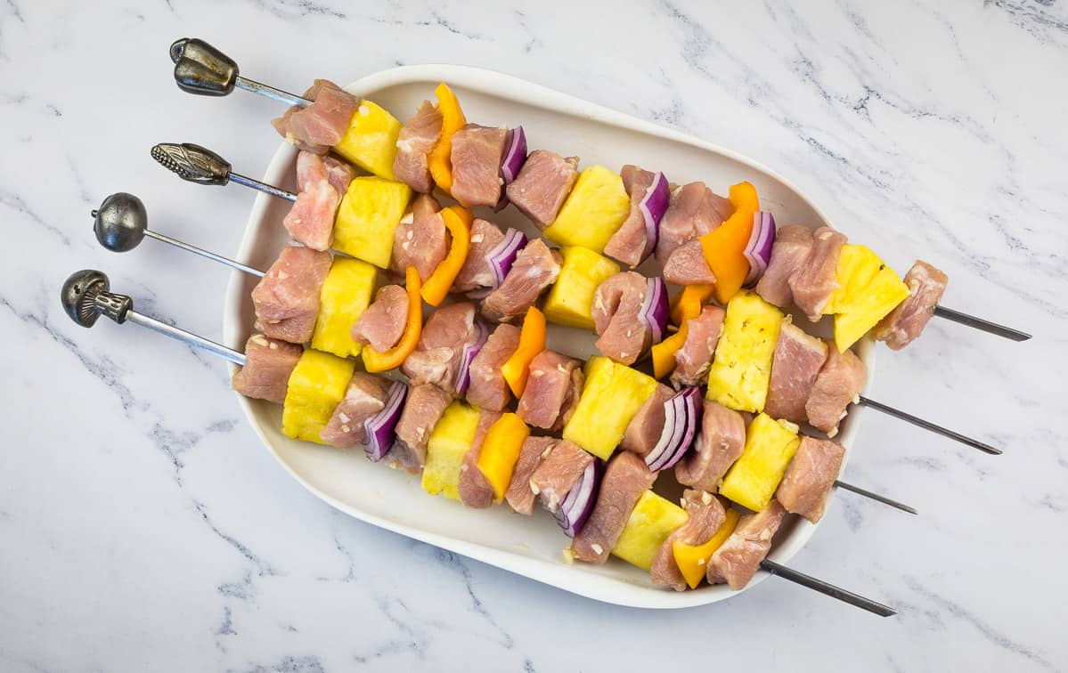 Uncooked Smoked Pork and Pineapple Kabobs on a white plate.