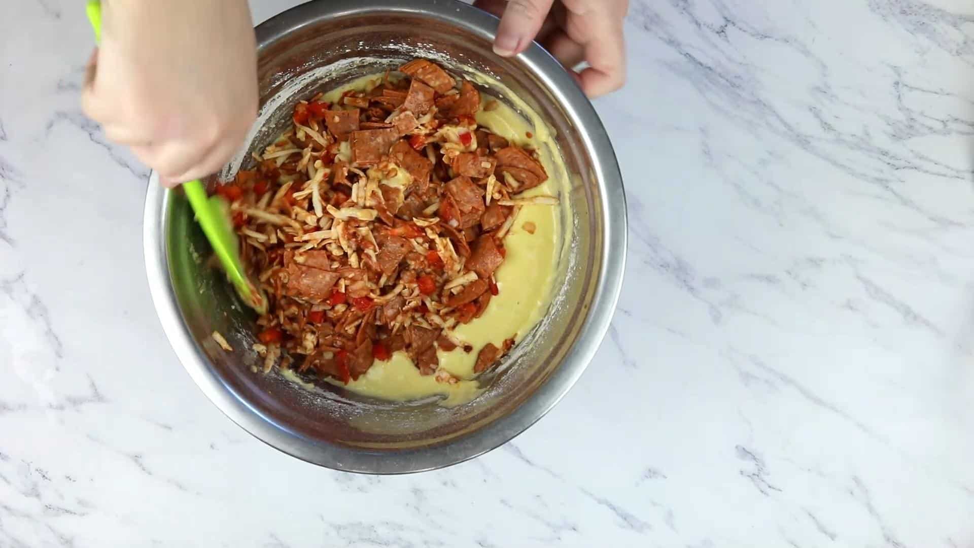 Combining the pizza ingredients and the batter.