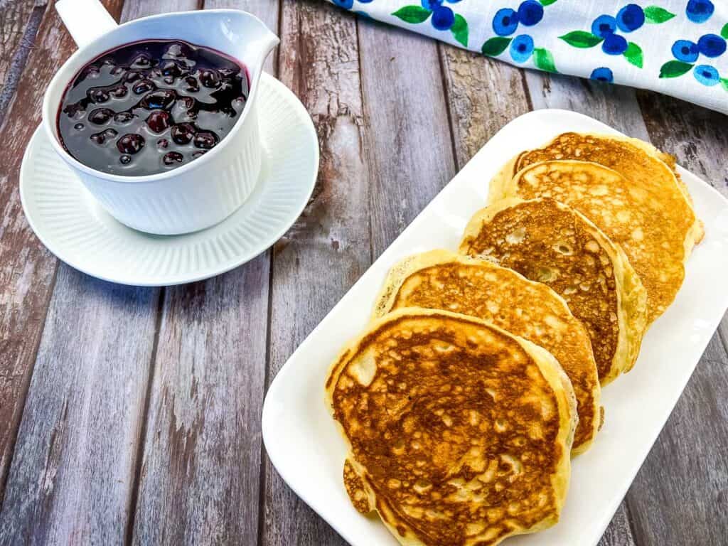 Buttermilk Blackstone Pancakes on a platter with blueberry sauce in the background.