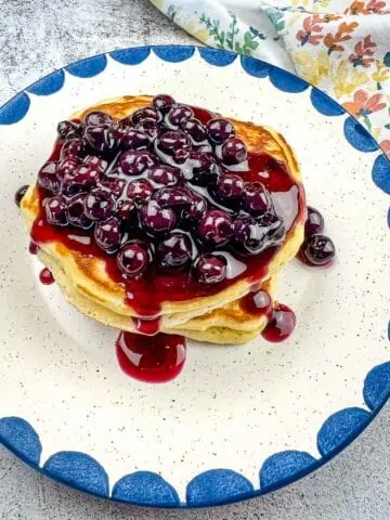 A stack of Blackstone Buttermilk pancakes with blueberry syrup on a plate.