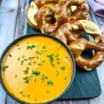 Guinness Cheese Dip in a black bowl with pretzels nearby.