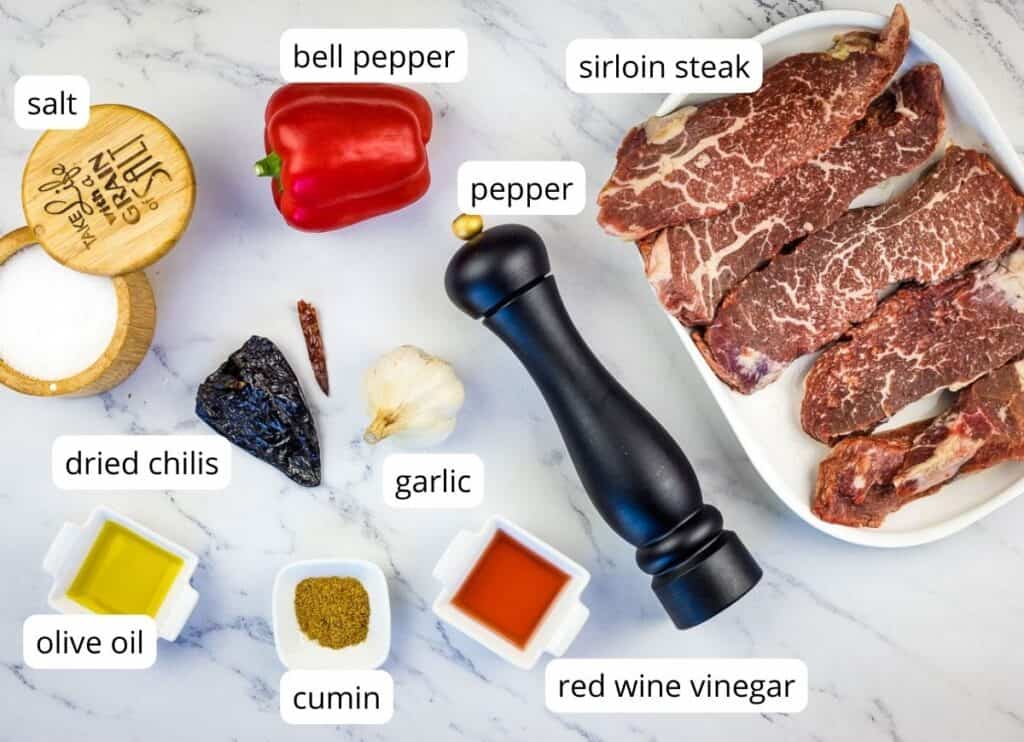 Labeled ingredients to make grilled steak skewers with mojo rojo sauce.