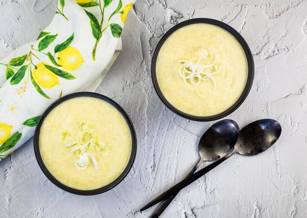 A top-down shot of two bowls of Cream of Leek and Green Garlic Soup.