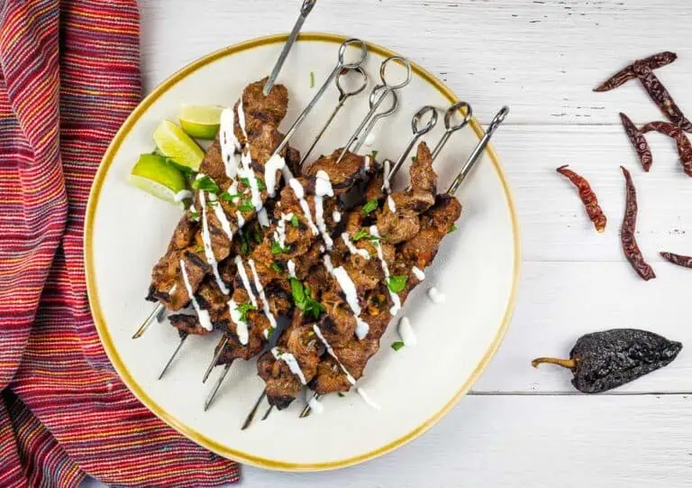 Mexican steak skewers with mojo rojo, served on a plate with lime and chilies.