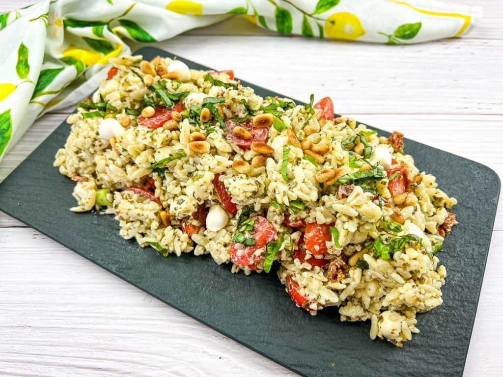 A plate of pesto orzo salad with tomatoes and pine nuts.