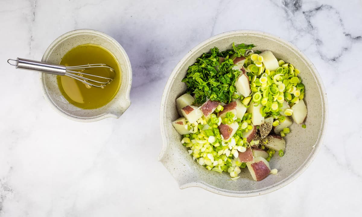 Potato Salad with Herb ingredients in a bowl next to the vinaigrette.