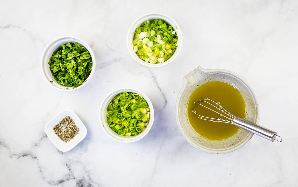 The potato salad vinaigrette next to the chopped herbs.