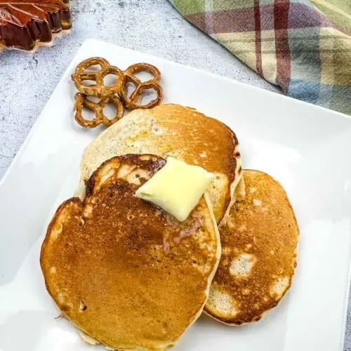 Pretzel pancakes on a plate with butter and syrup in the background.